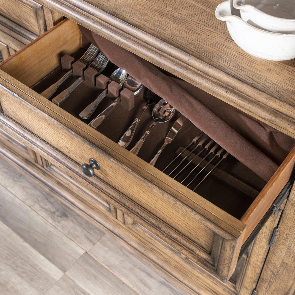 An open wooden drawer lined with brown felt, organized with silverware including forks, spoons, and knives.