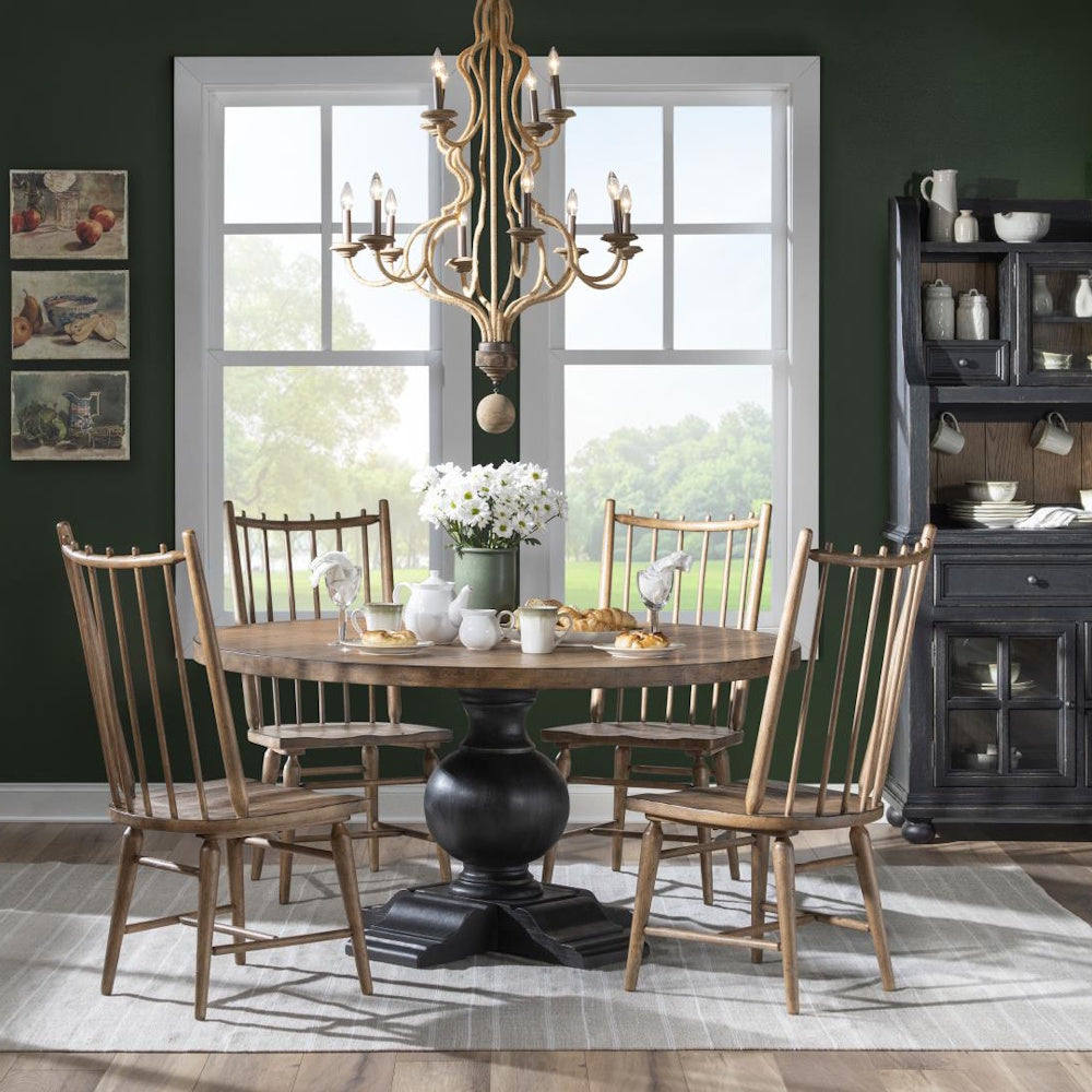 Wooden spindle-back chairs around a round dining table with a chandelier above in a green room.