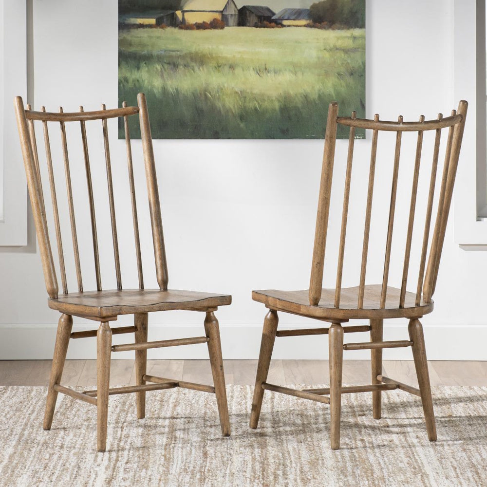 Two wooden spindle-back chairs on a textured rug in front of a painting of a countryside field.