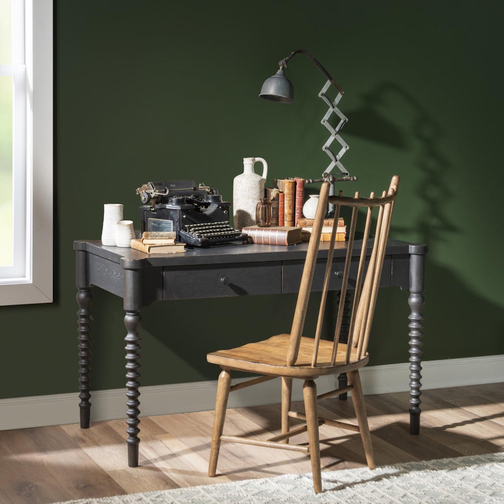 A wooden spindle-back chair tucked into a dark grey desk with a vintage typewriter against a green wall.