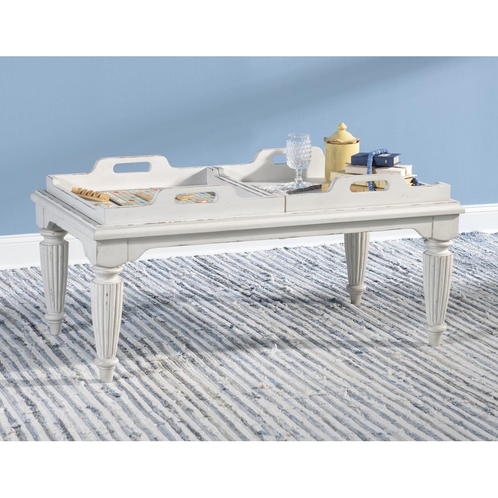 White distressed tray-top cocktail table styled with a board game and decor on a striped blue rug.