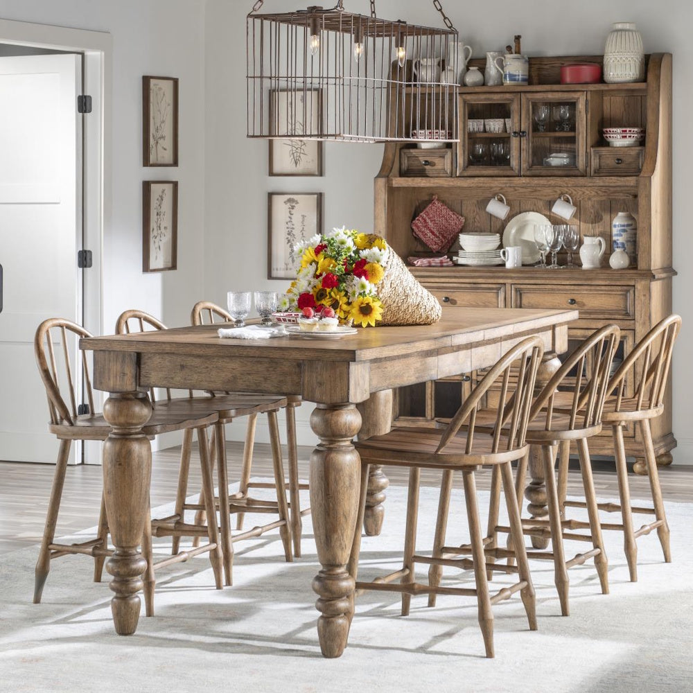 Rustic wooden dining set with spindle-back stools, a flower centerpiece, and a large hutch in the background.