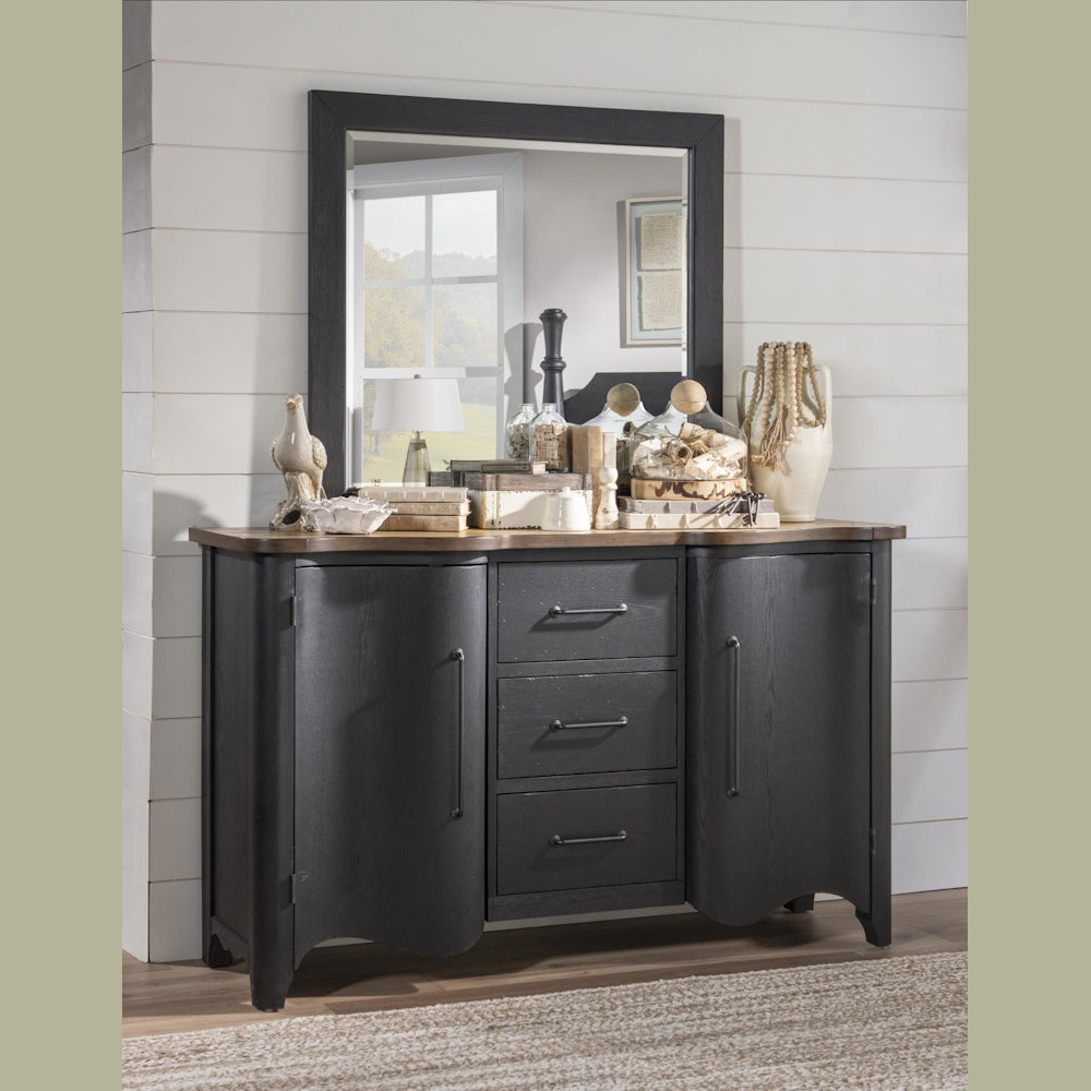 Rustic black wooden dresser with mirror and wood top in a farmhouse bedroom setting.