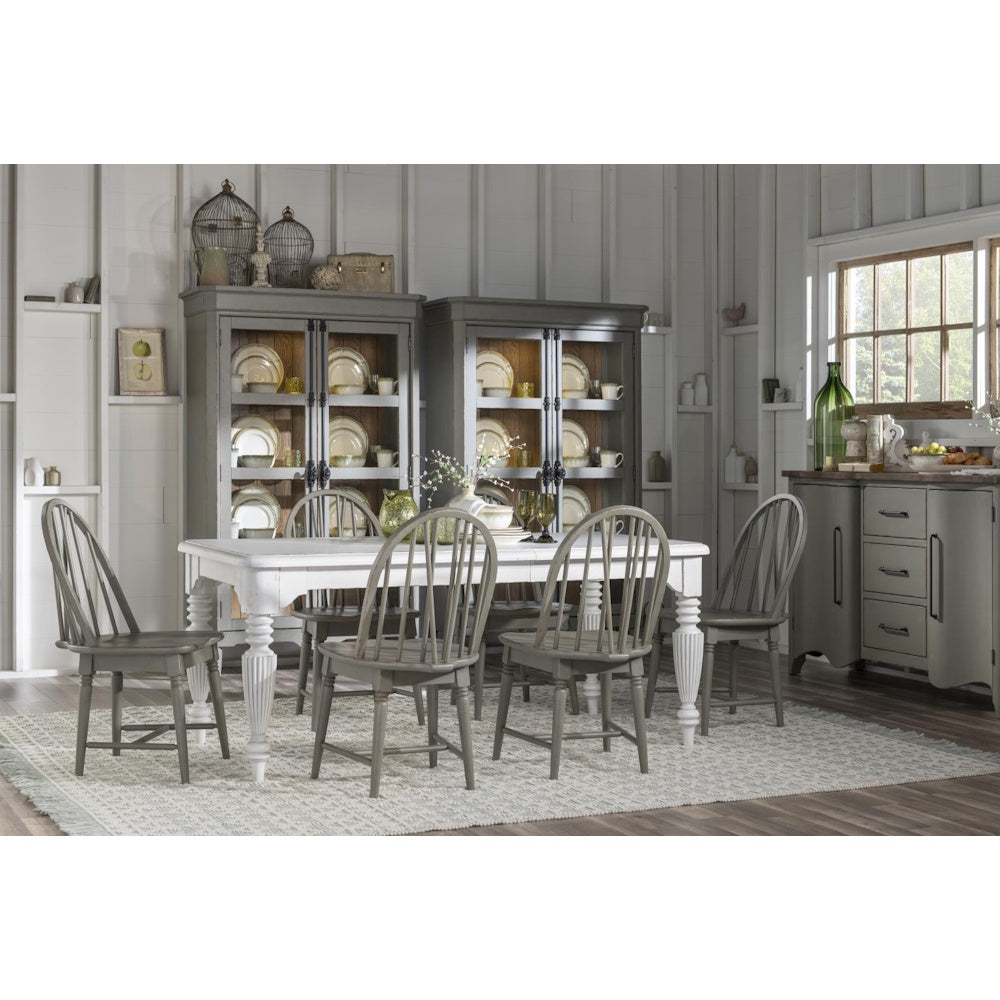 Light gray Windsor chairs around a white dining table in a bright farmhouse dining room with display cabinets.