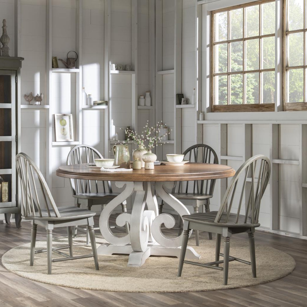 Light gray Windsor chairs gathered around a round pedestal dining table in a bright farmhouse dining room.