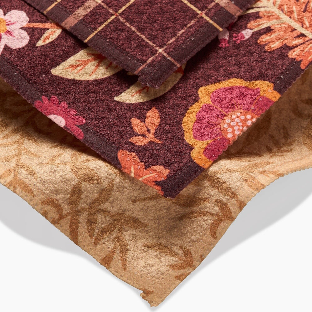 A close-up of folded fall dishcloths featuring plaid, floral, and leaf patterns in warm autumn tones.