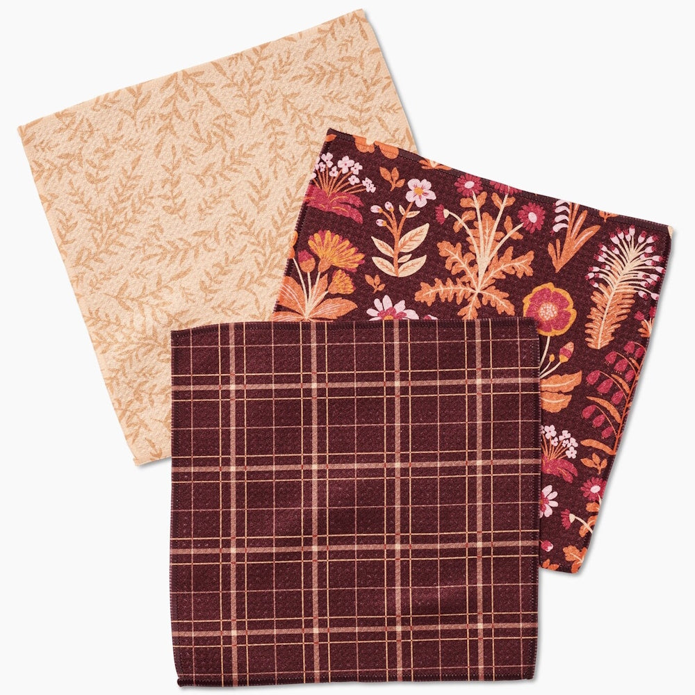 A set of three autumn-themed dishcloths featuring a tan leaf pattern, a floral print, and a brown plaid design.