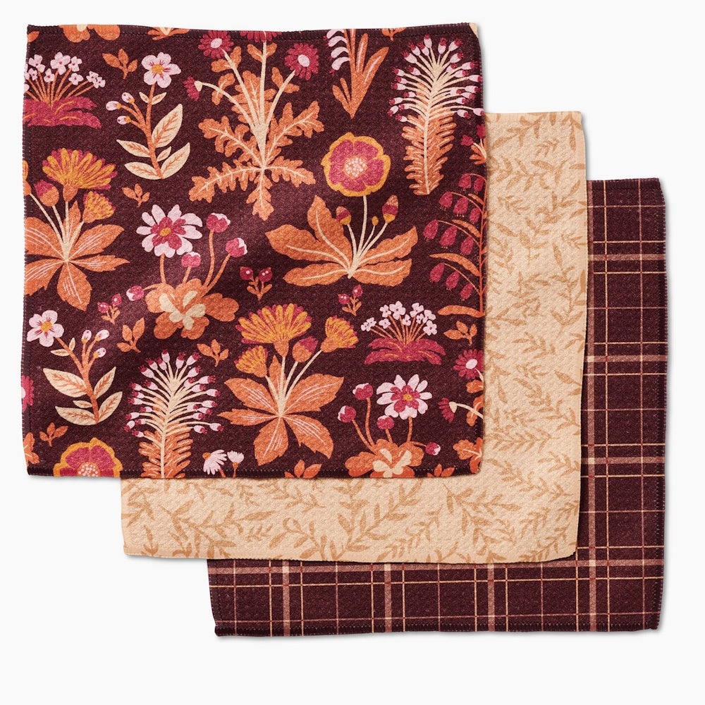 A set of three square dishcloths featuring autumn patterns: a floral botanical print, a tan vine print, and a dark plaid.