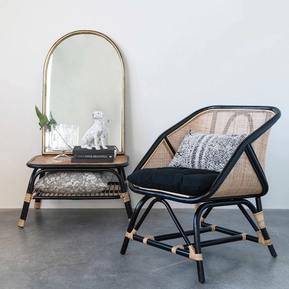 Hand-painted ceramic dog figurine on a side table with a gold arch mirror and modern black rattan accent chair.