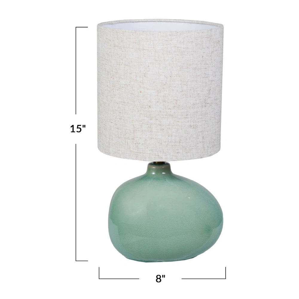 A 15-inch table lamp featuring a green crackle-glaze stoneware base and a neutral linen drum shade on a white background.