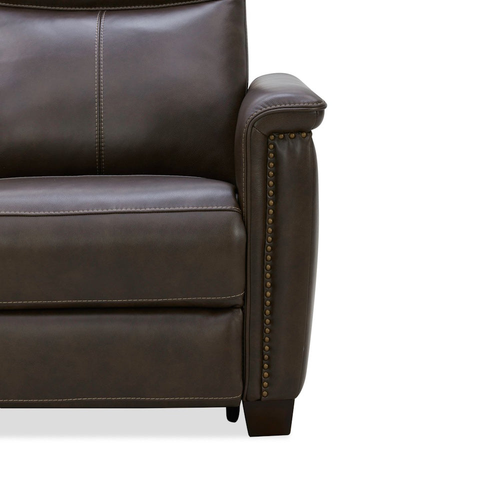 Close-up of a brown leather armchair with nailhead trim and decorative stitching.