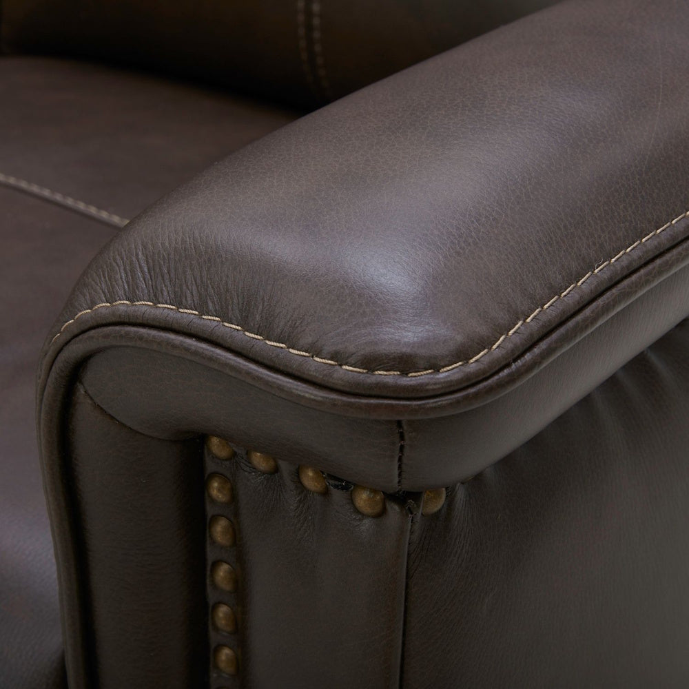 Close-up of a brown leather armchair with decorative stitching and brass nailhead trim.