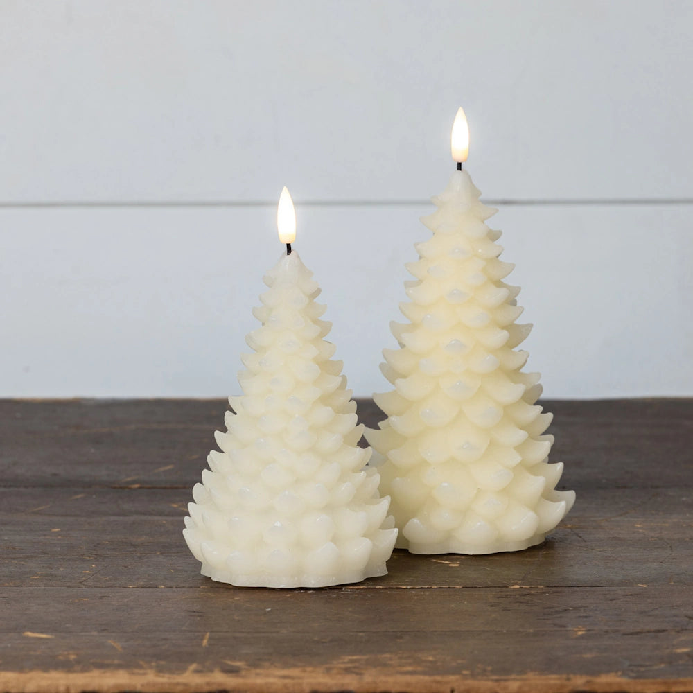 Two cream-colored, tree-shaped flameless candles glowing on a wooden surface against a light backdrop.