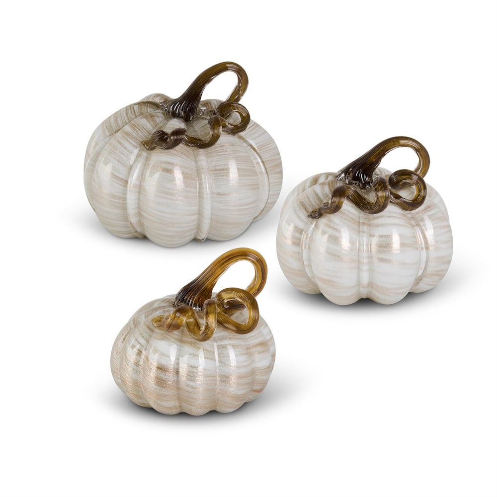 A set of three cream and gold swirled hand-blown glass pumpkins with curled brown stems on a white background.
