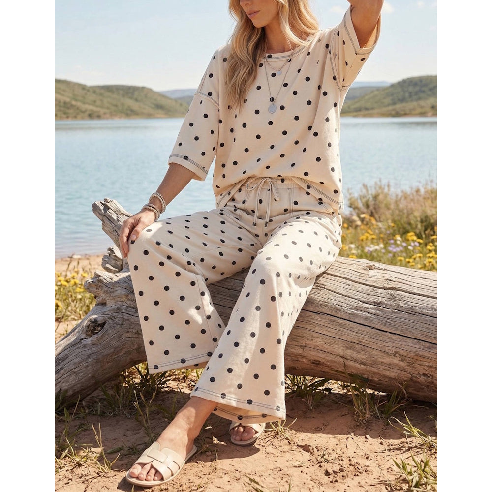 Woman sitting on a log in a cream and black polka dot short-sleeve top and wide-leg pants set.