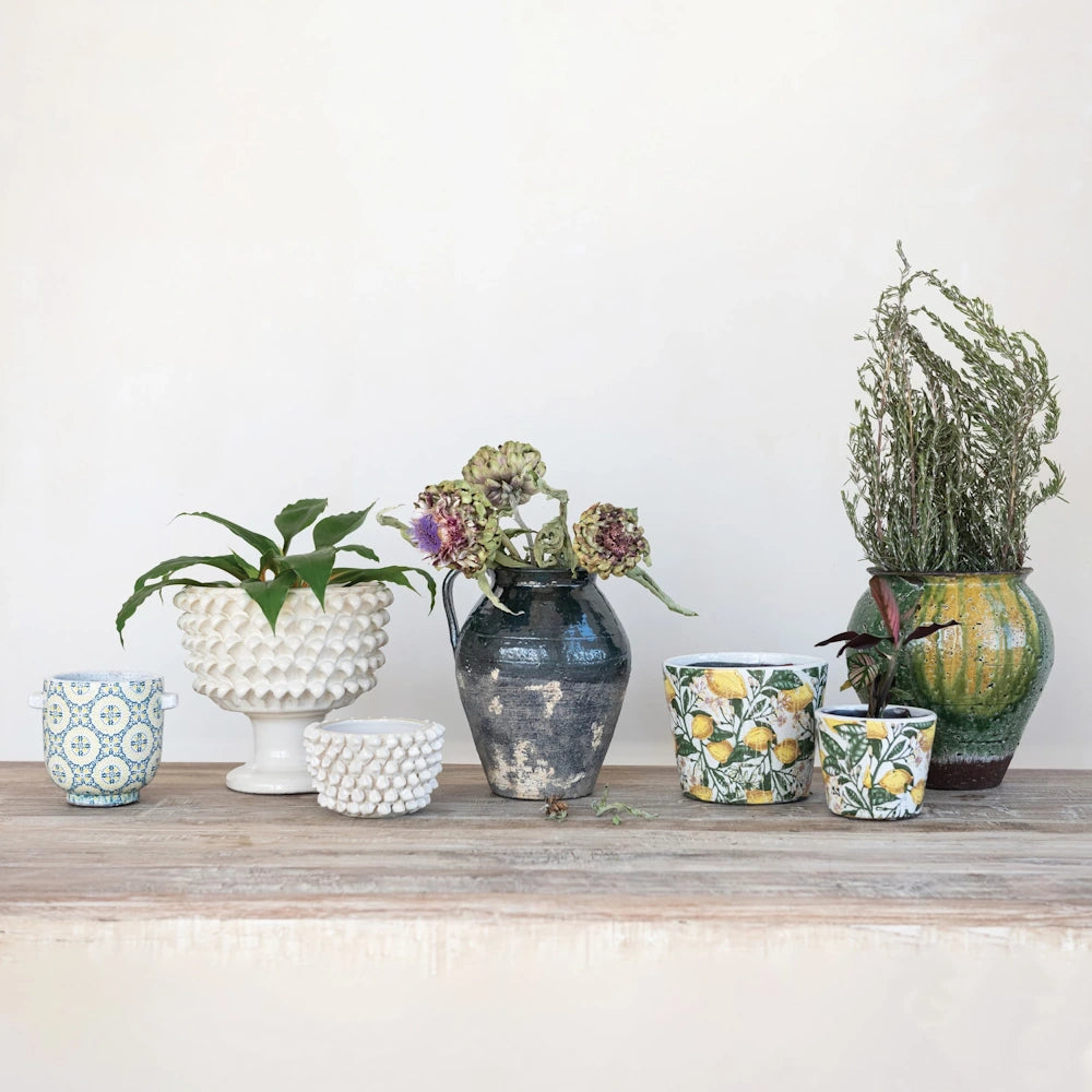 Assorted decorative ceramic planters, textured white pots, and vintage vases with dried flowers on a rustic wooden table.
