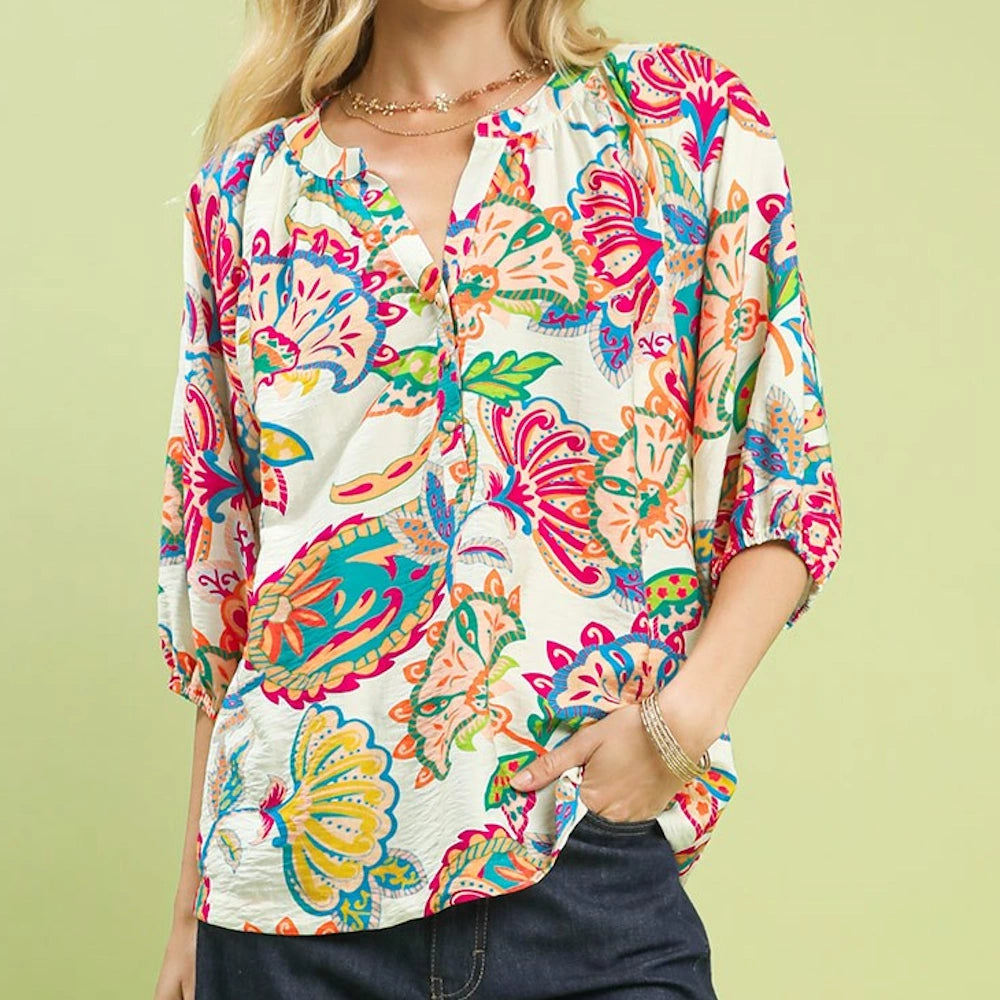 A woman in a vibrant, colorful floral blouse and dark denim pants, with a lime green background.