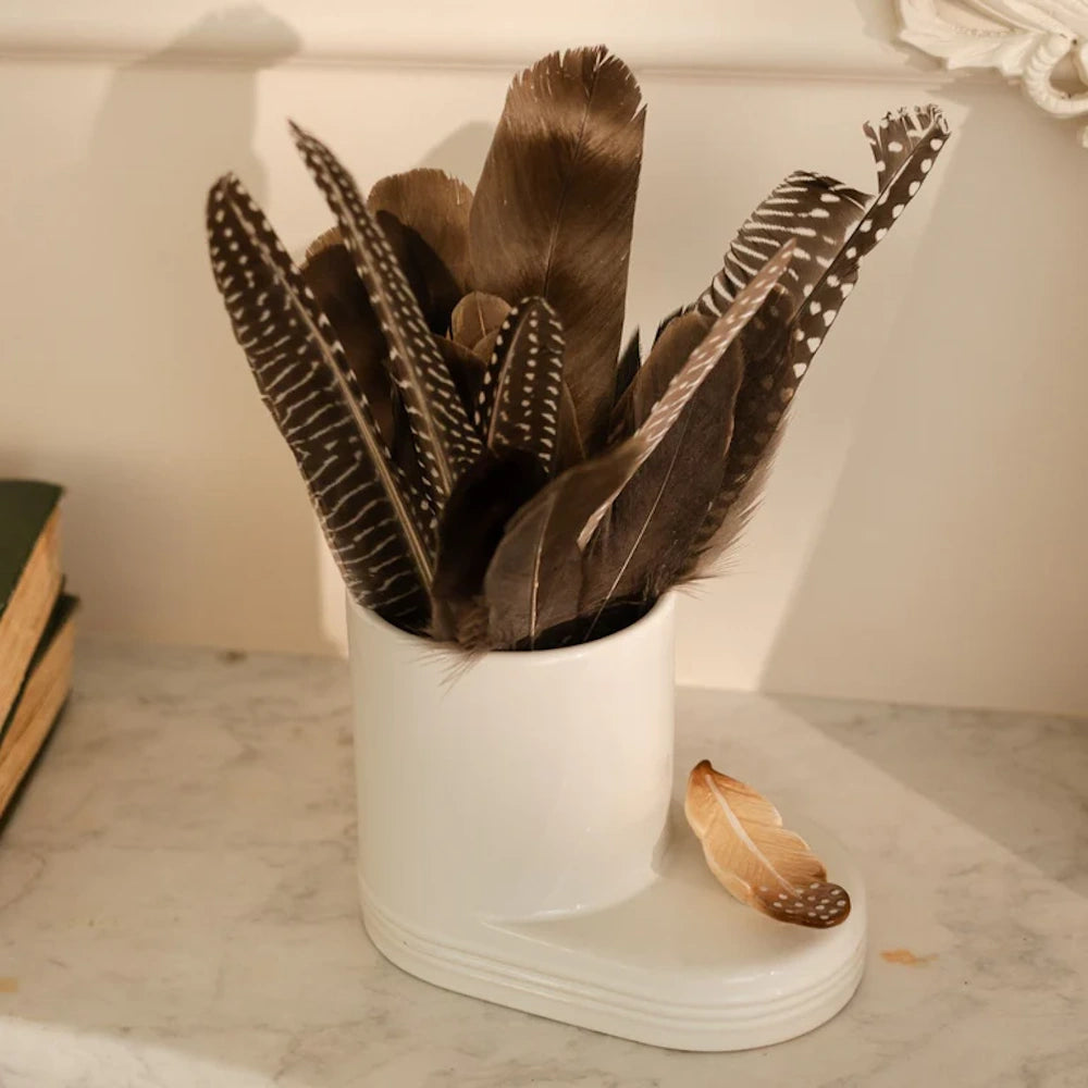 A collection of patterned brown and spotted feathers in a white ceramic holder on a marble surface.