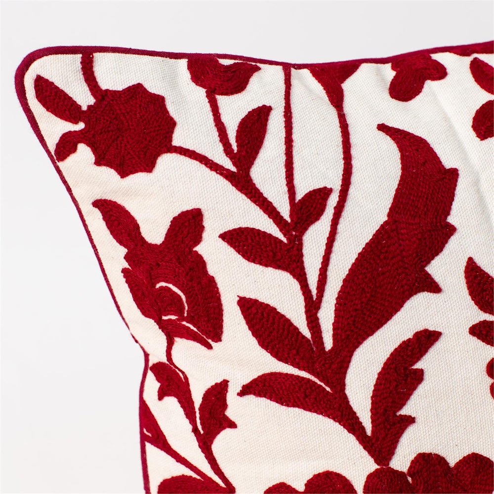 Close-up of an off-white pillow featuring intricate red embroidered floral crewelwork and piping.