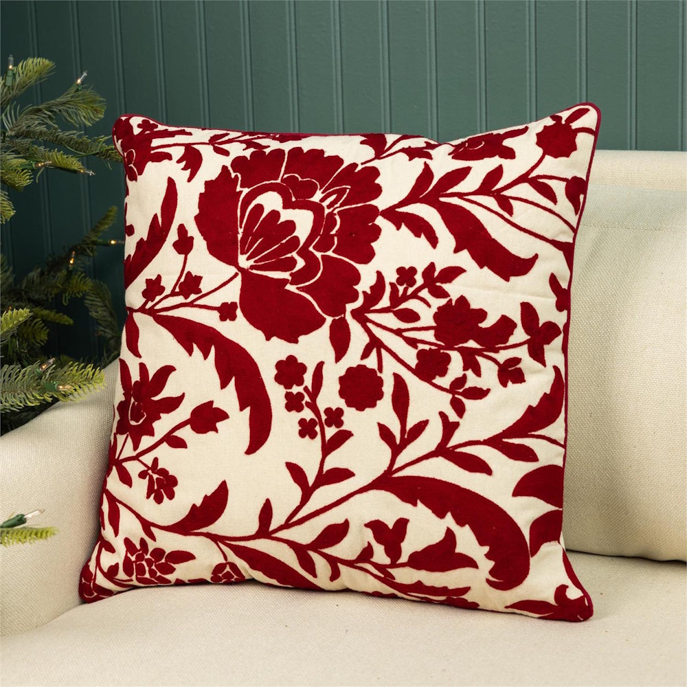Cream throw pillow featuring a red embroidered floral pattern resting on a beige sofa.
