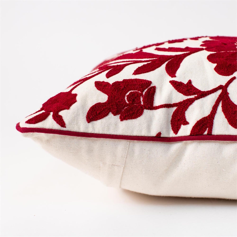 Side view of a white fabric pillow featuring raised red floral embroidery and matching red piping.