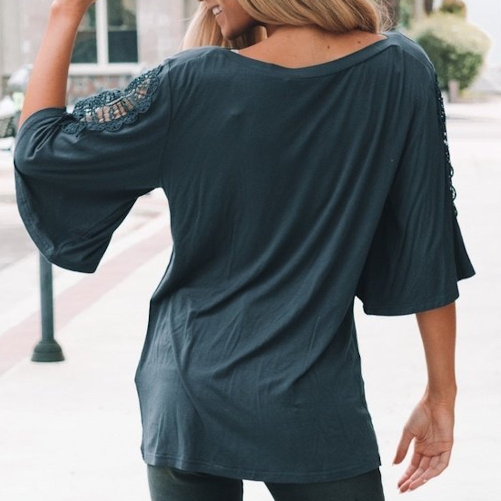 Back view of a woman wearing a dark teal short-sleeve top with lace crochet detailing on the shoulders.