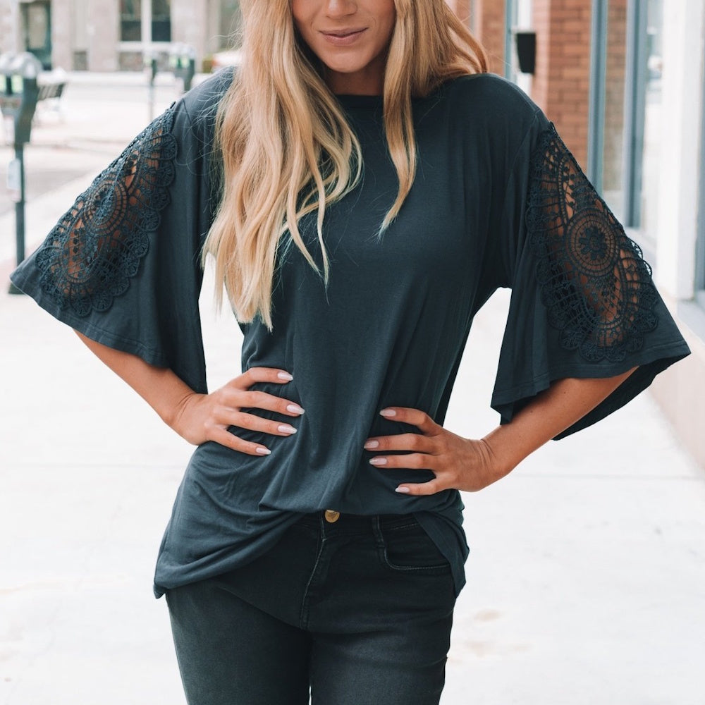 A woman wearing a charcoal t-shirt with distinctive lace-paneled bell sleeves and black jeans.