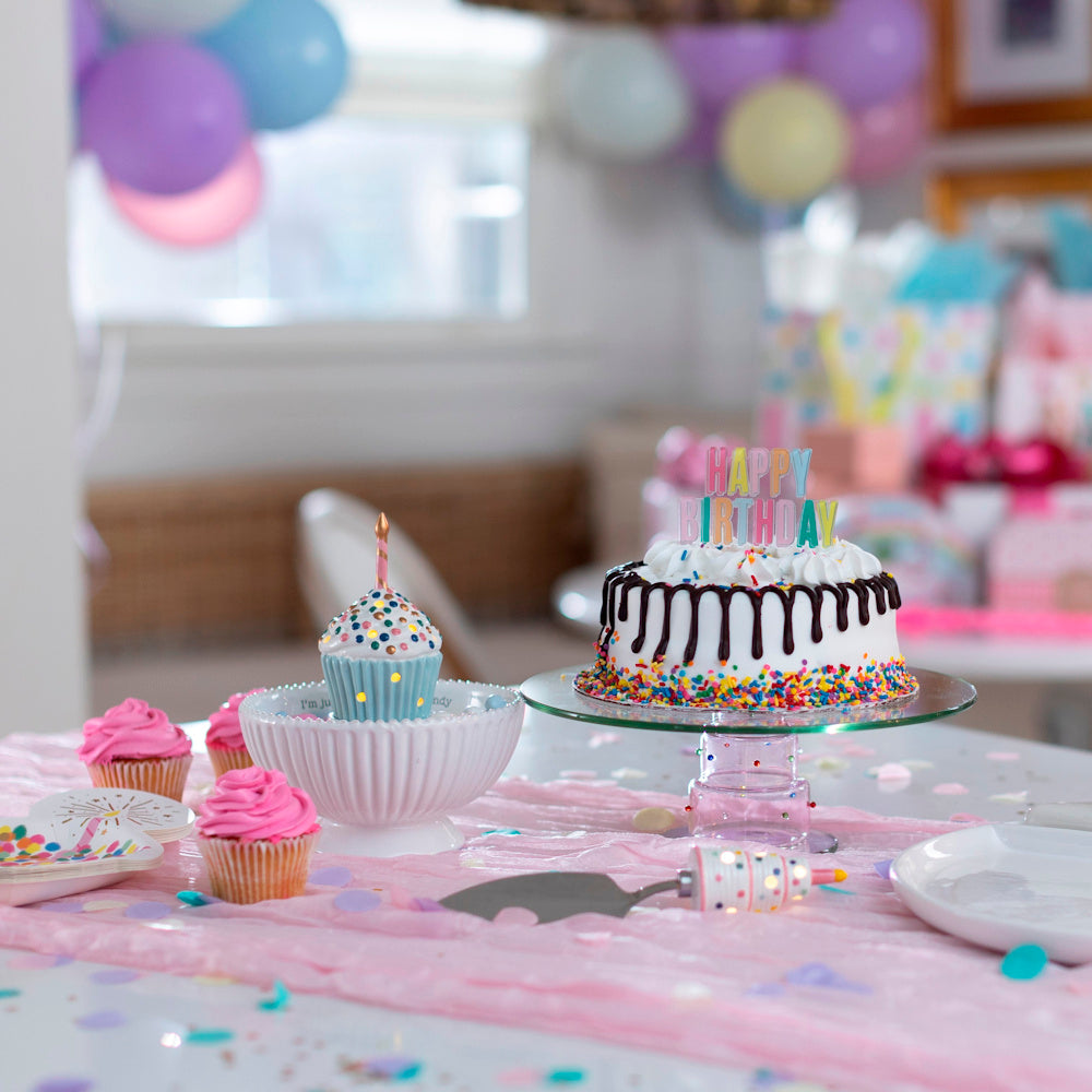 Birthday party table with sprinkle cake, pink cupcakes, and a light-up ceramic cupcake sitter on a pink runner.