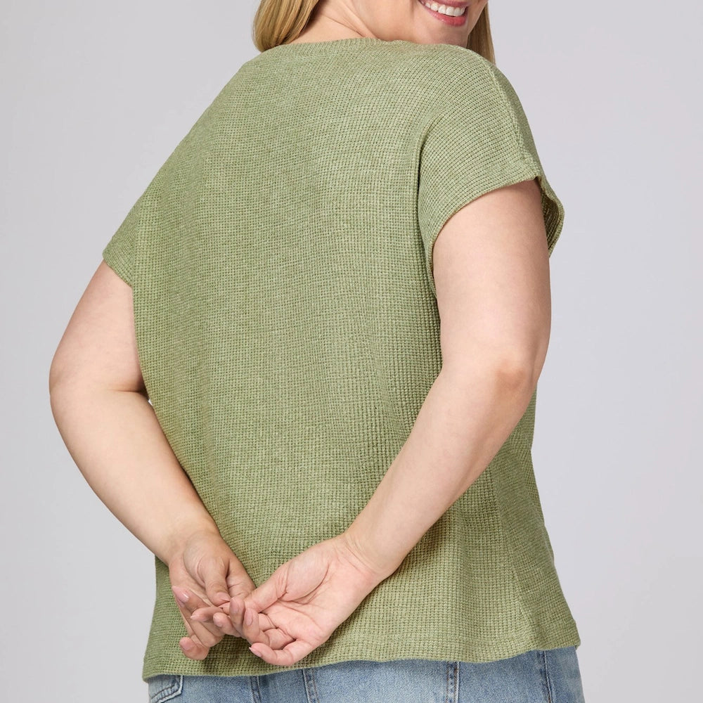 Woman from behind in a sage green drop-sleeve waffle knit top and jeans with her hands clasped behind her back.