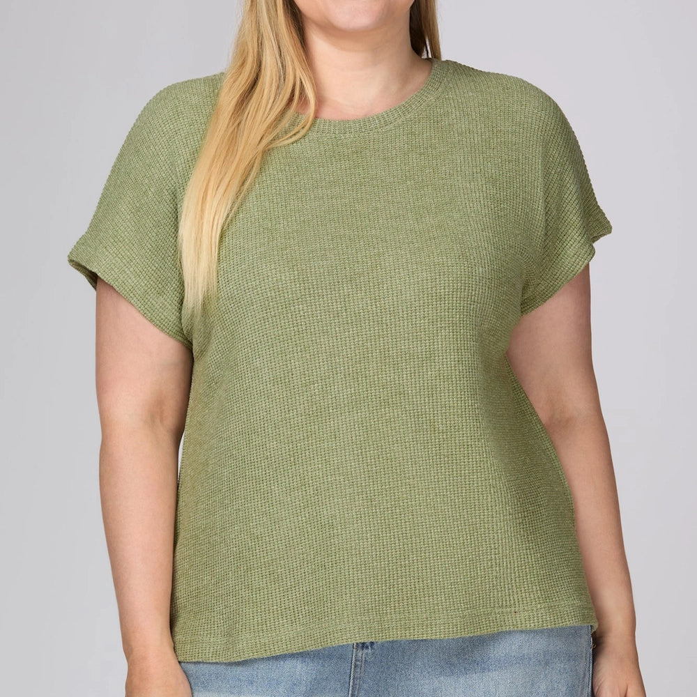 Woman wearing an olive green drop sleeve round neck knit top and light wash blue jeans.