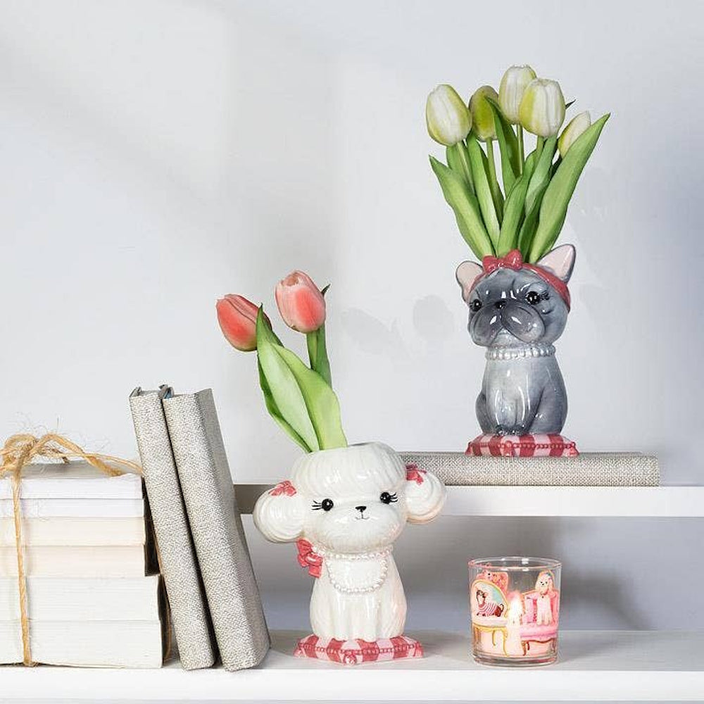 Two dog-shaped ceramic vases holding tulips on white shelves next to books and a candle holder.