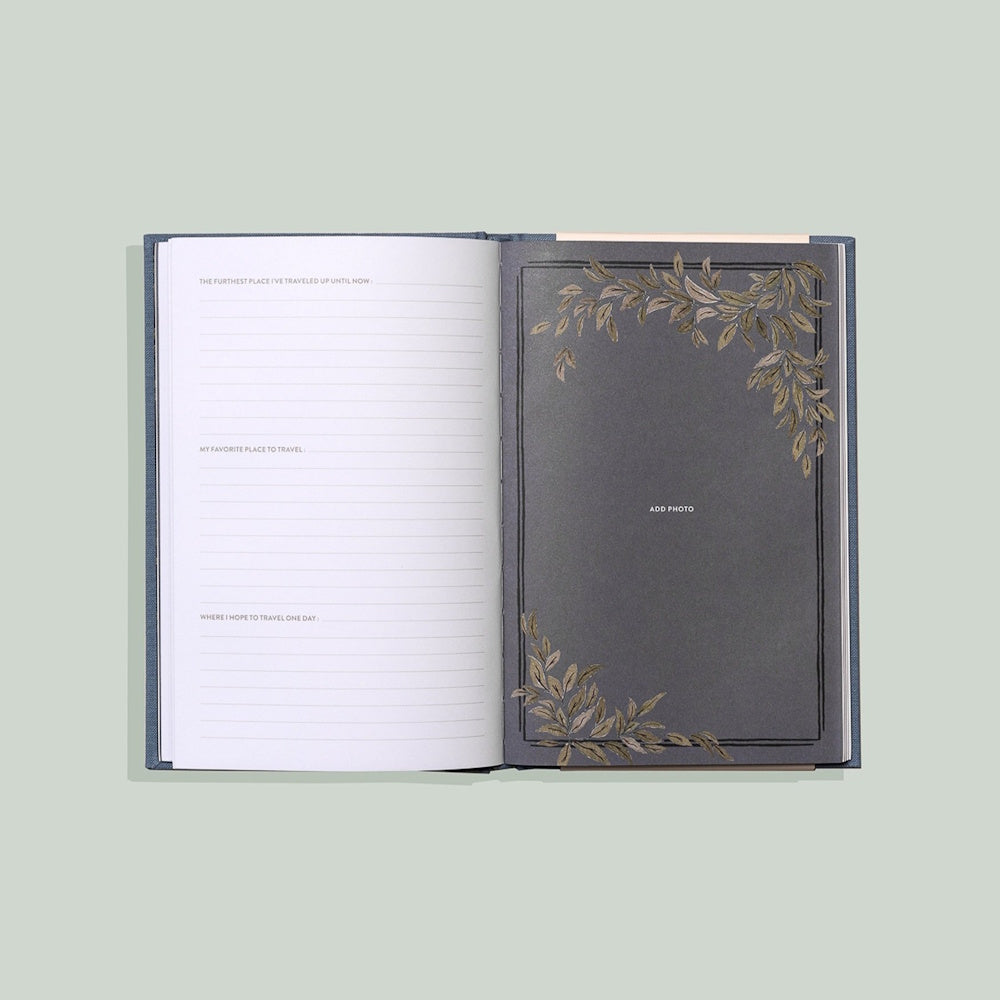 Open journal with travel prompts on the left and a dark photo page with gold leaf illustrations on the right.