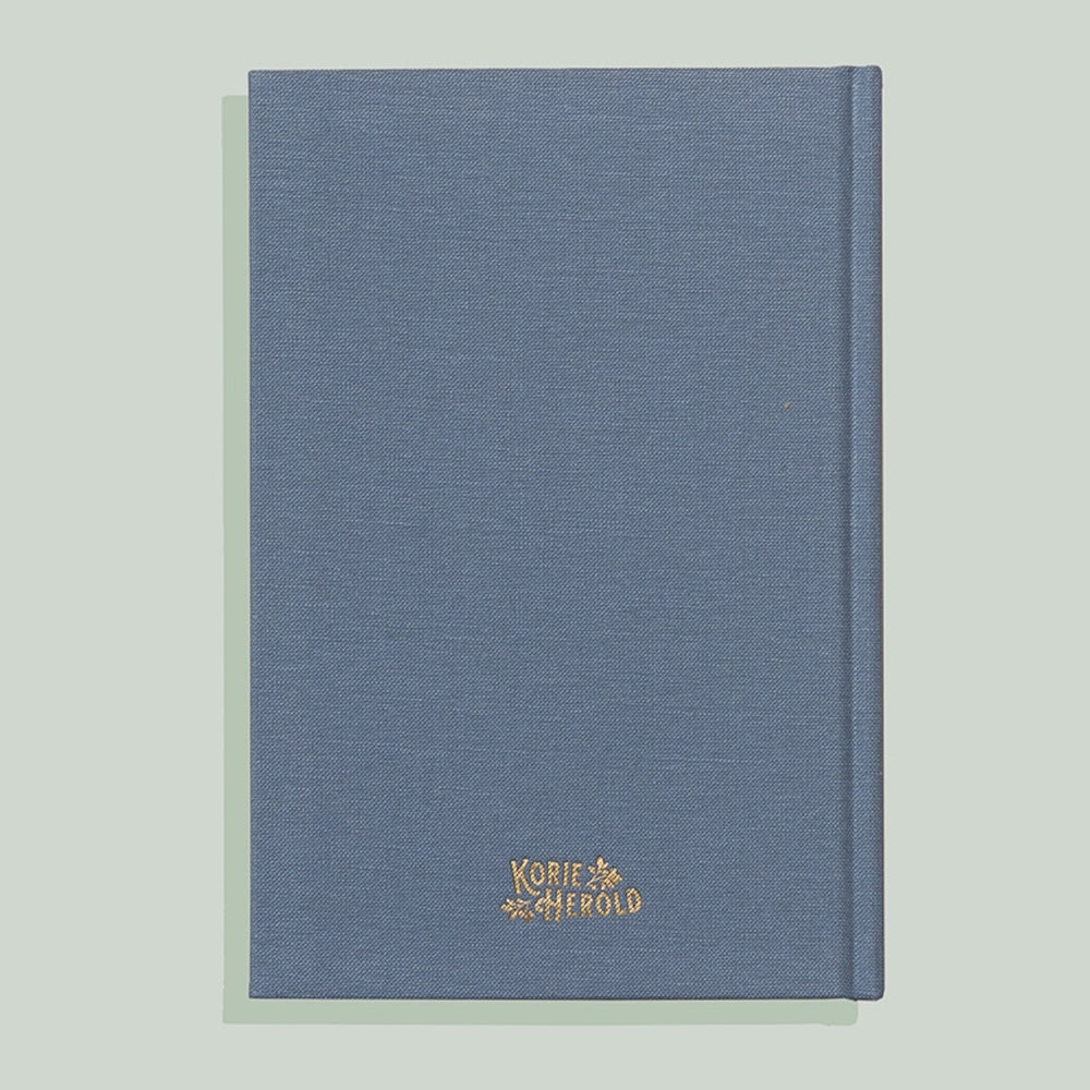 Back cover of a blue linen-textured journal with a gold "Korie Herold" logo centered at the bottom.