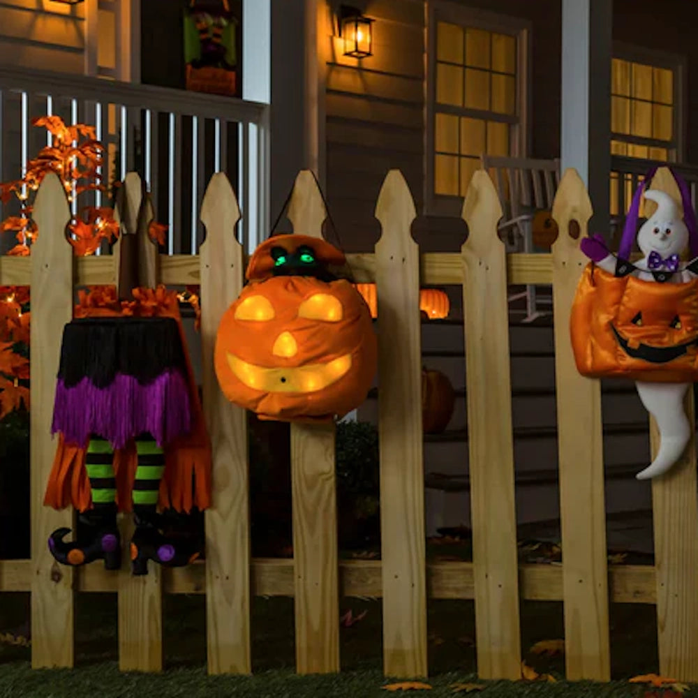 Halloween door decor with witch legs, a glowing pumpkin, and a ghost hanging on a wooden fence.