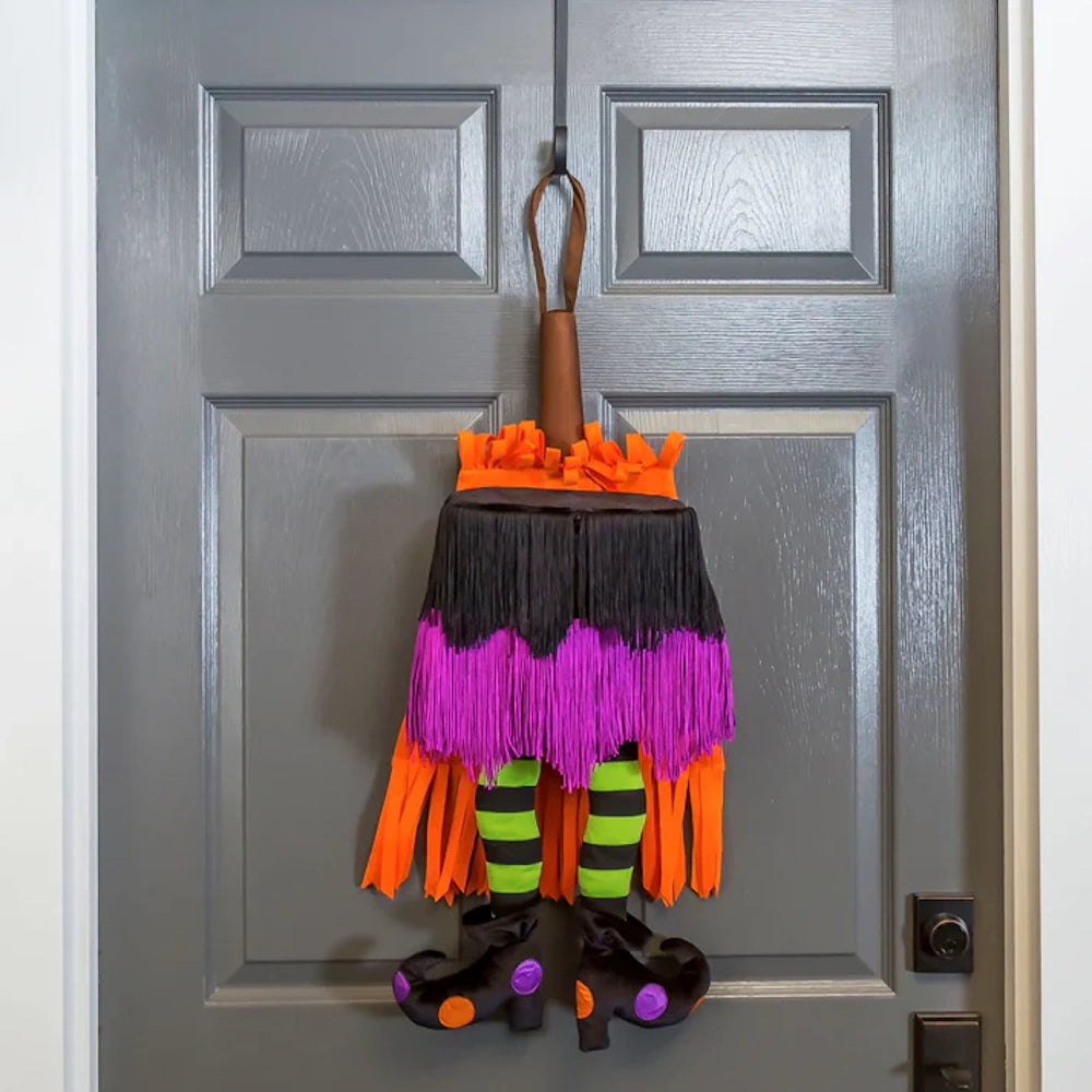 Whimsical Halloween witch door decor featuring a fringe skirt, striped legs, and curled boots hanging on a door.