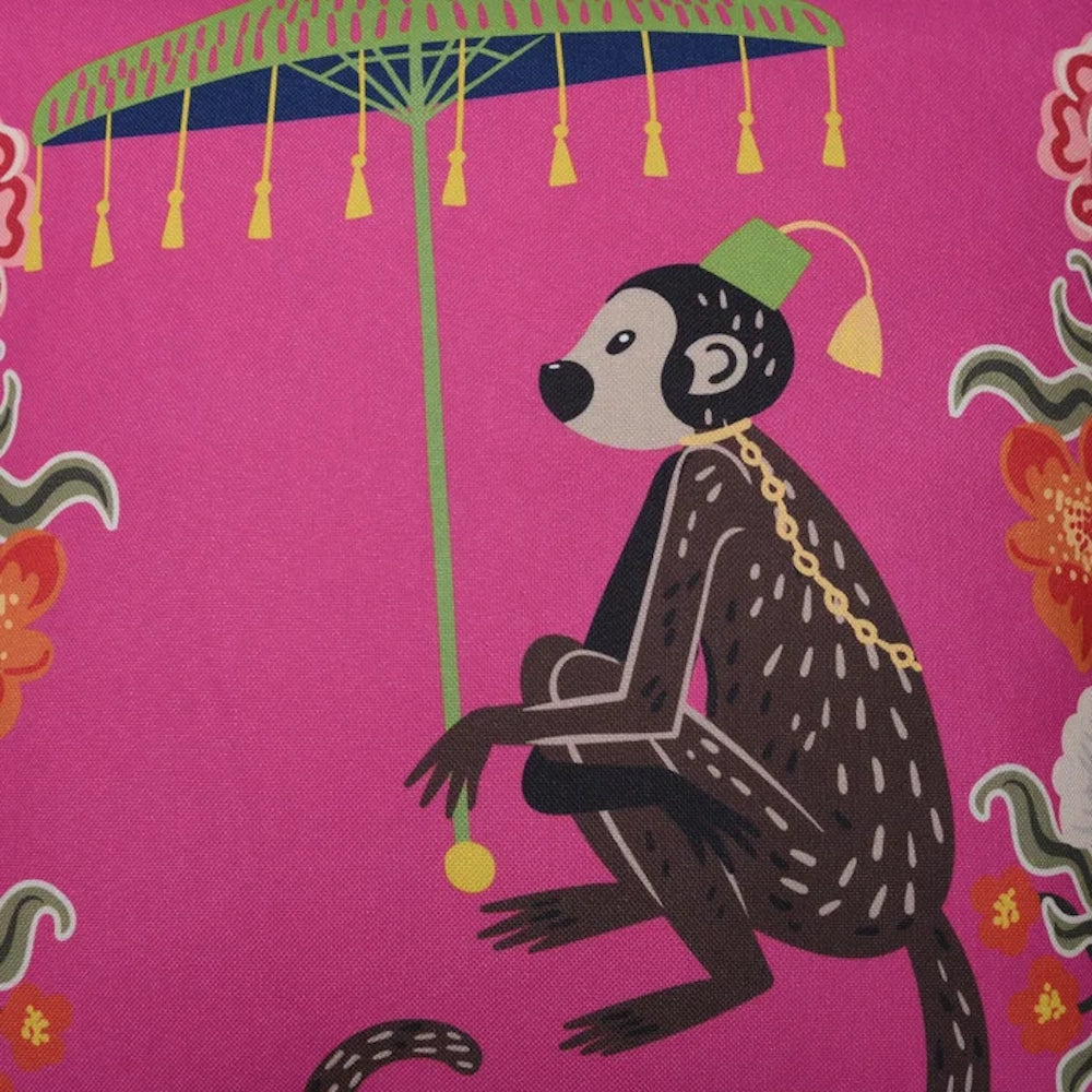 Close-up of a pink decorative pillow featuring a whimsical monkey illustration with a green umbrella.