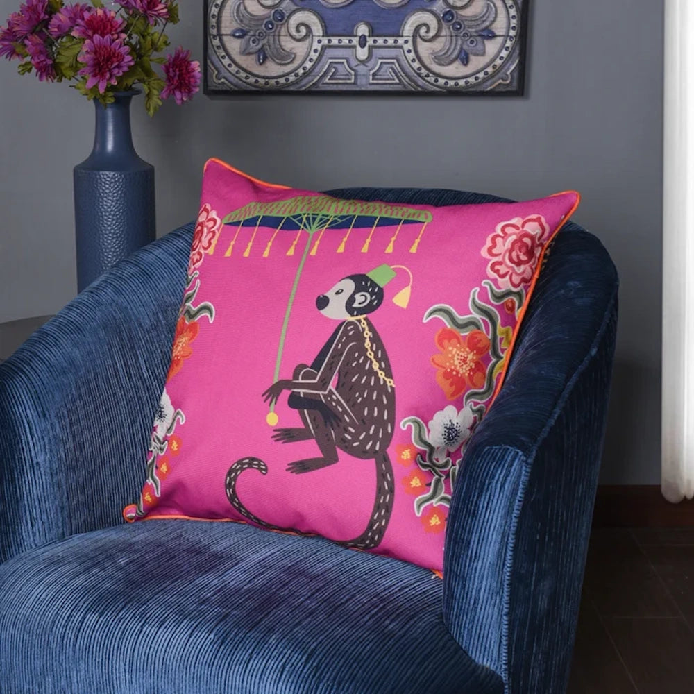 Pink monkey print decorative throw pillow with floral accents on a blue corduroy armchair.