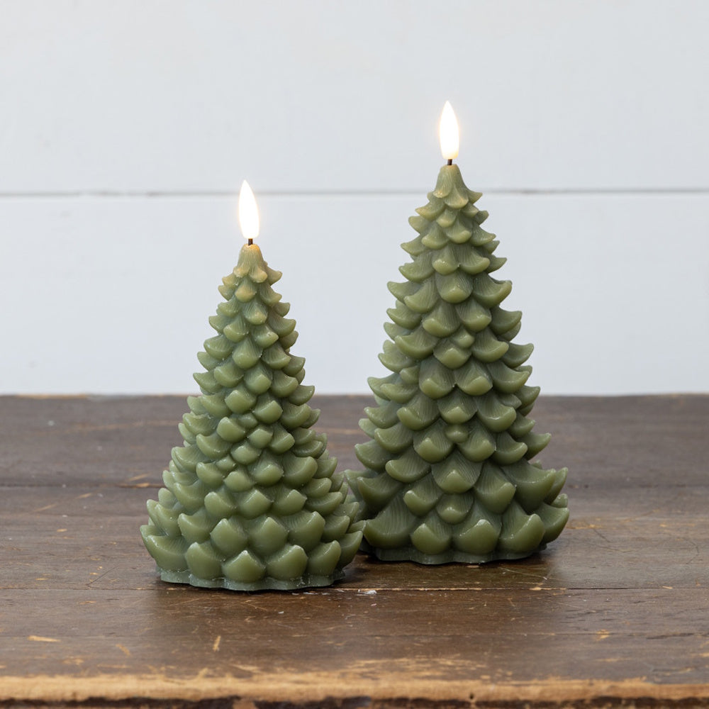 Two lit dark green Christmas tree-shaped LED candles standing on a rustic wooden table.