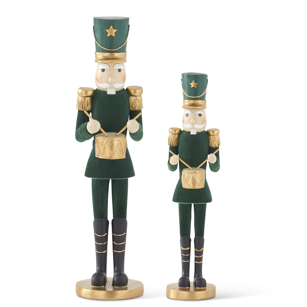 Two dark green velvet nutcrackers in gold-trimmed uniforms holding drumsticks and playing drums on a white background.