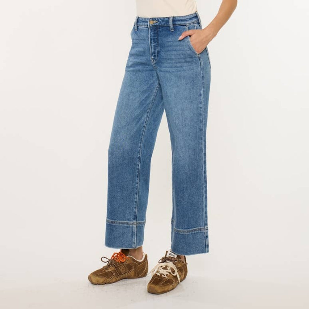Side view of high-rise cropped wide-leg blue jeans styled with brown sneakers on a white background.