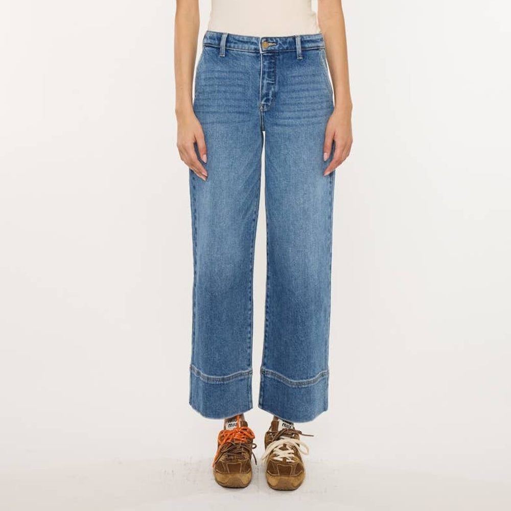 Woman wearing high-rise cropped wide-leg blue jeans with wide stitched hems and casual brown sneakers.
