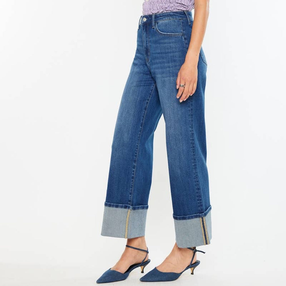 Side view of high-rise wide-leg blue jeans with large cuffed hems, paired with denim pointed heels.