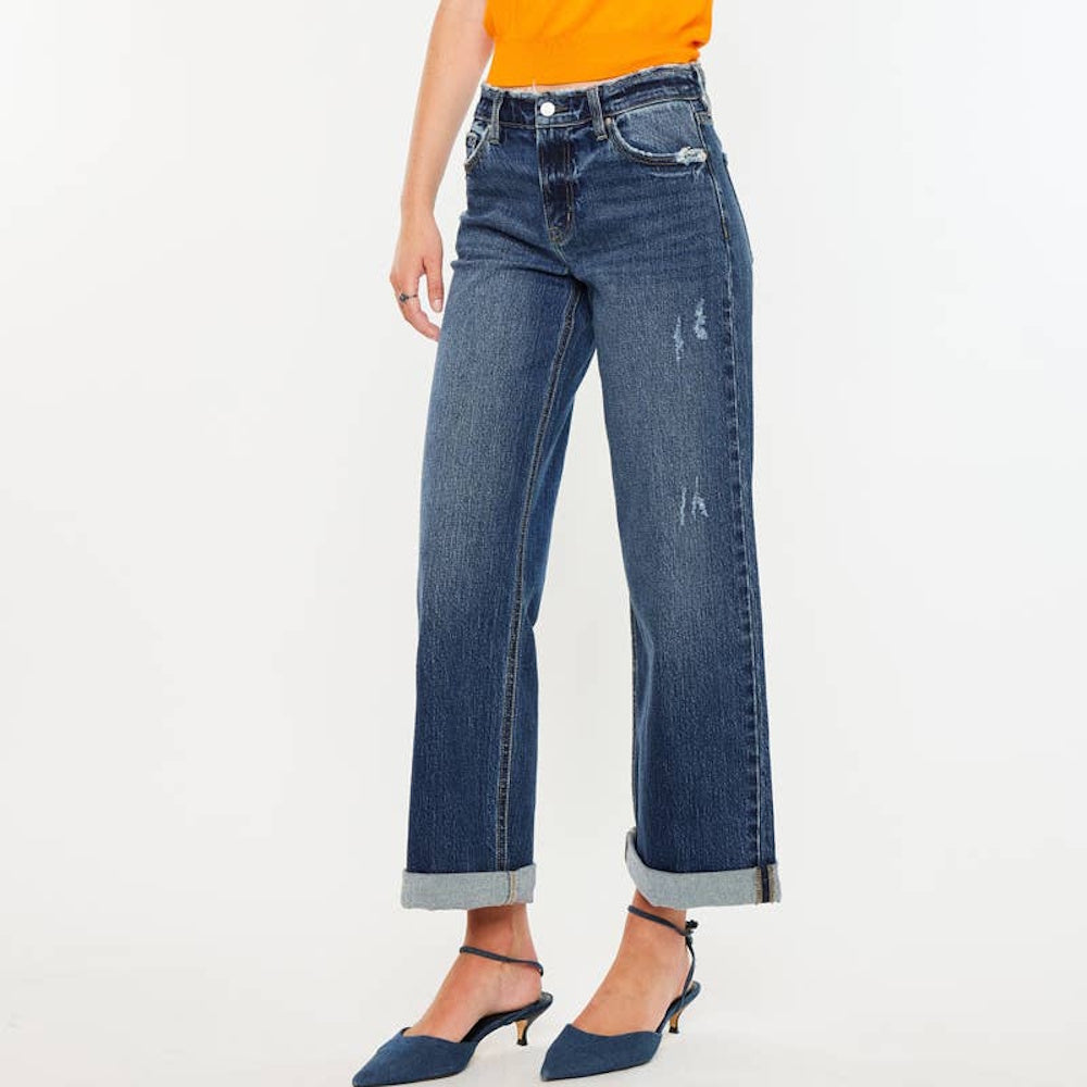 Side view of high-rise wide-leg blue jeans with cuffed hems and light distressing, paired with blue heels.