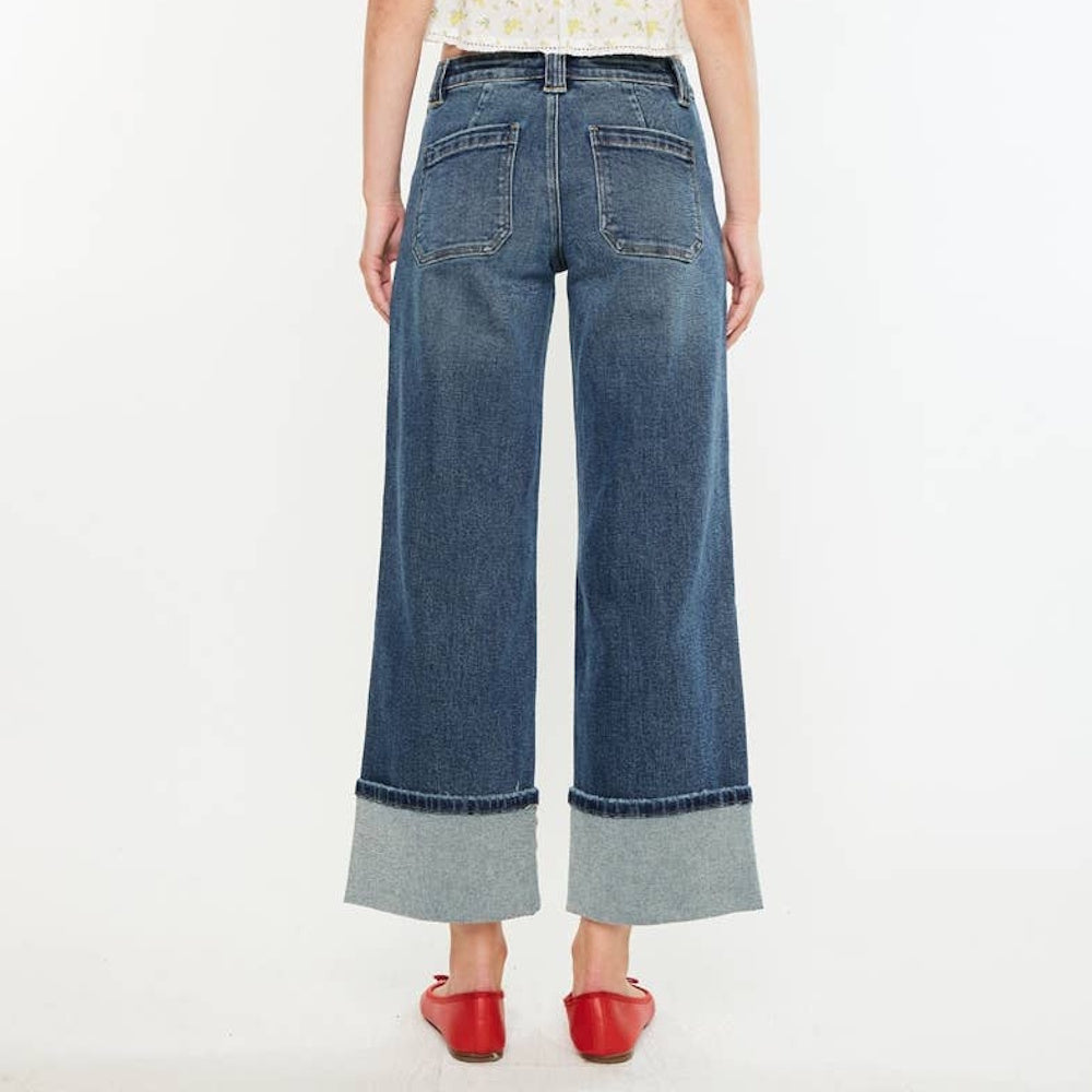 Back view of wide-leg blue denim jeans featuring wide cuffed hem design, patch pockets, and red shoes.