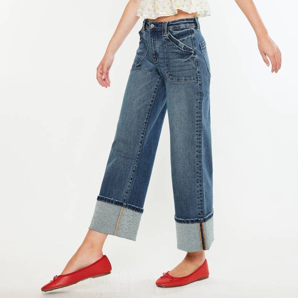 A person wearing wide-leg cuffed blue jeans with front patch pockets and red ballet flats.
