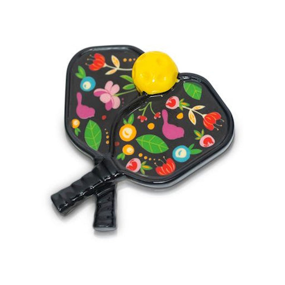 A colorful enamel pin featuring two crossed, floral-patterned pickleball paddles and a yellow ball.
