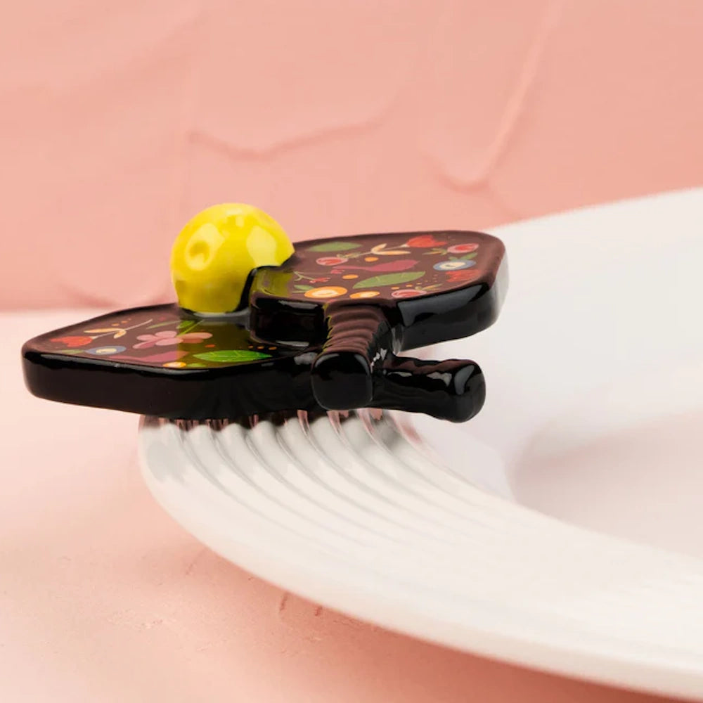Two pickleball paddles decorated with flowers and a yellow ball, serving as a decorative plate attachment.