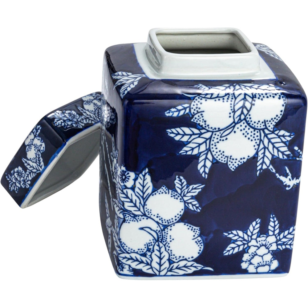 Square blue and white ceramic tea caddy with a floral and fruit pattern, its lid propped open on the side.