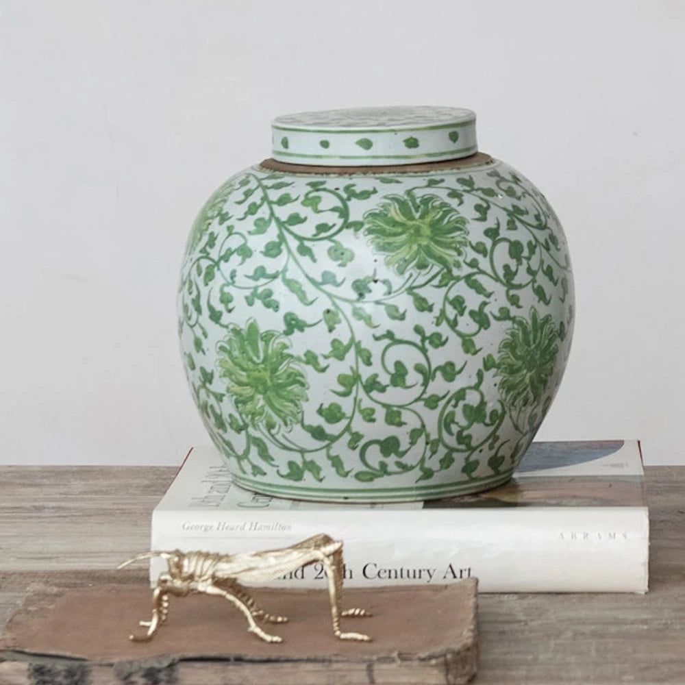 Decorative hand-painted stoneware ginger jar with green floral vine pattern, styled on books with a gold grasshopper.