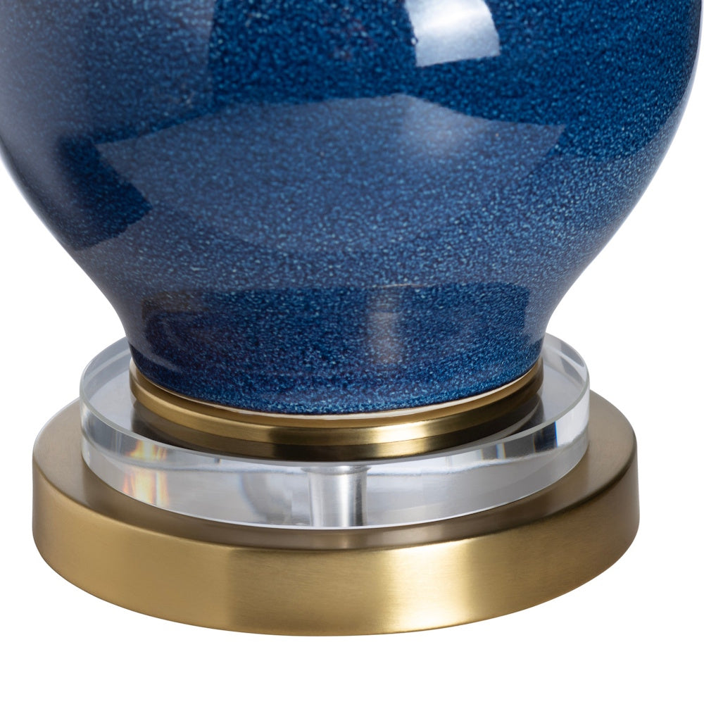 Close-up of a table lamp with a blue speckled ceramic base and a layered brass and clear acrylic stand.